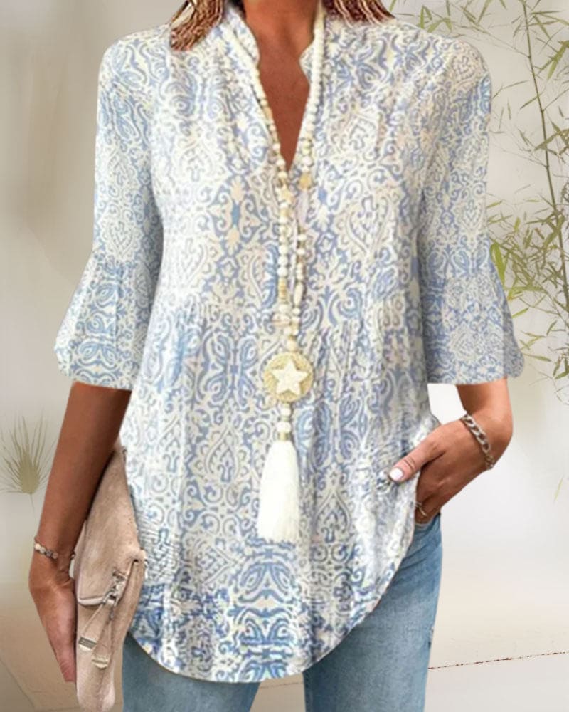 Kvinde iført lyseblå og hvid mønstret tunika med trekvartærmer, halskæde med stjernevedhæng, jeans og beige taske. Elegant bohemelook.