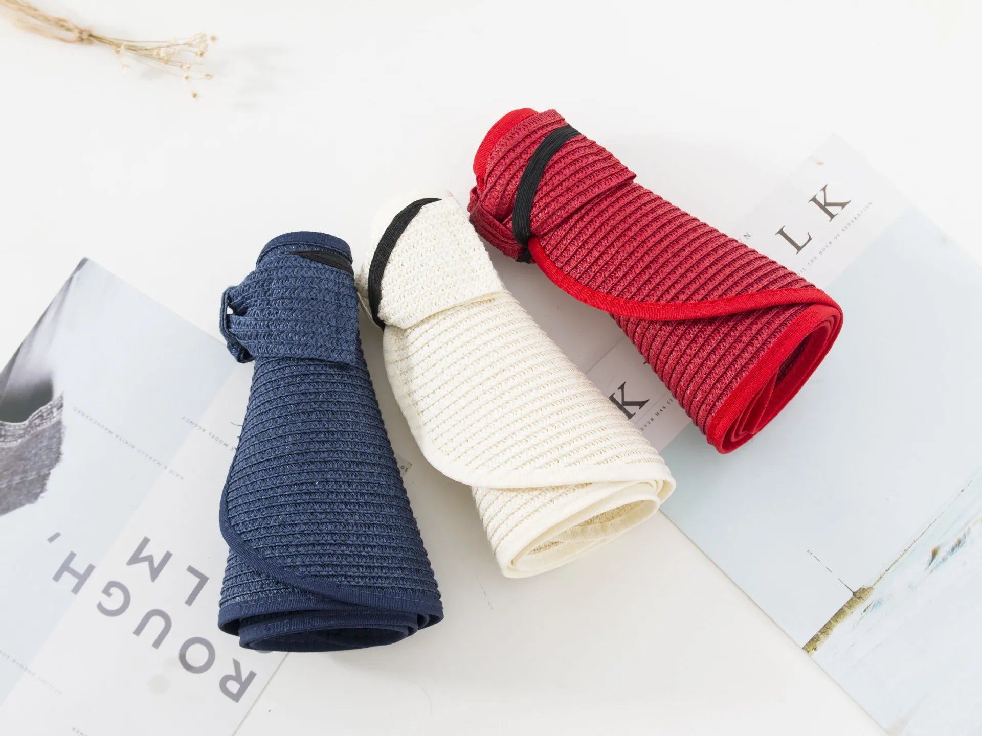 Tre sammenrullede elastiske bandager i blå, hvid og rød ligger på et bord med magasiner. Perfekt til sportsskader og støtte.