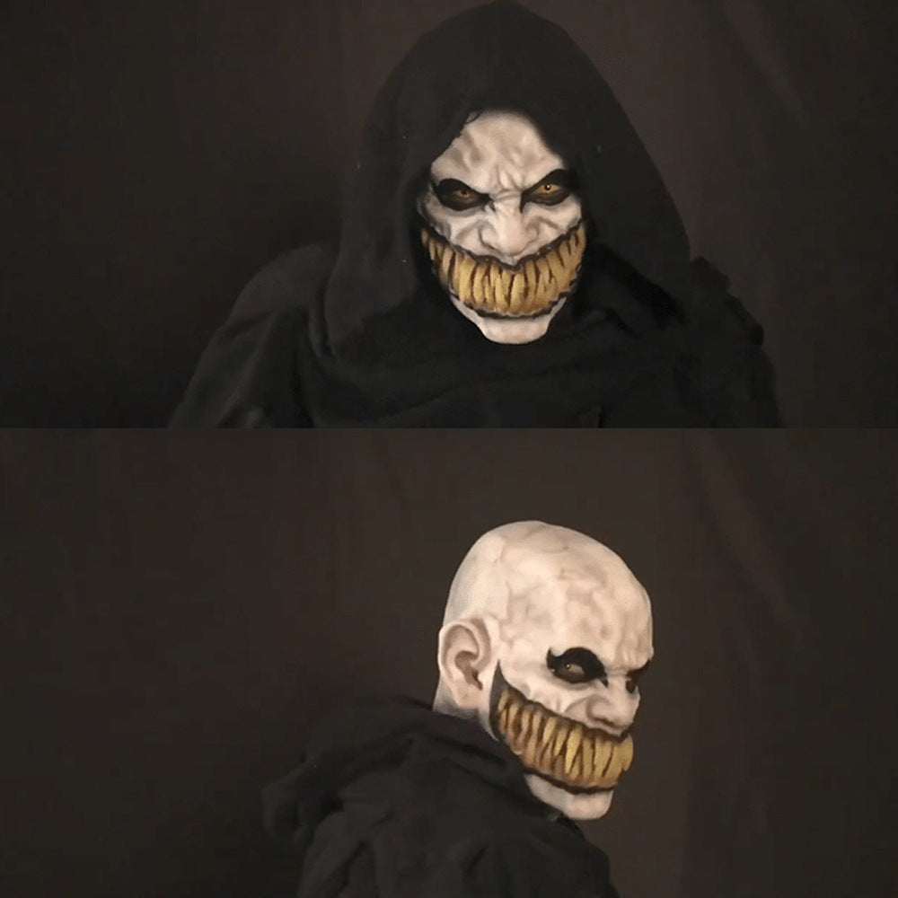 Sortklædt person med uhyggelig maske, skarpe tænder og hætte. Halloween kostume, skræmmende ansigt, mørk baggrund.
