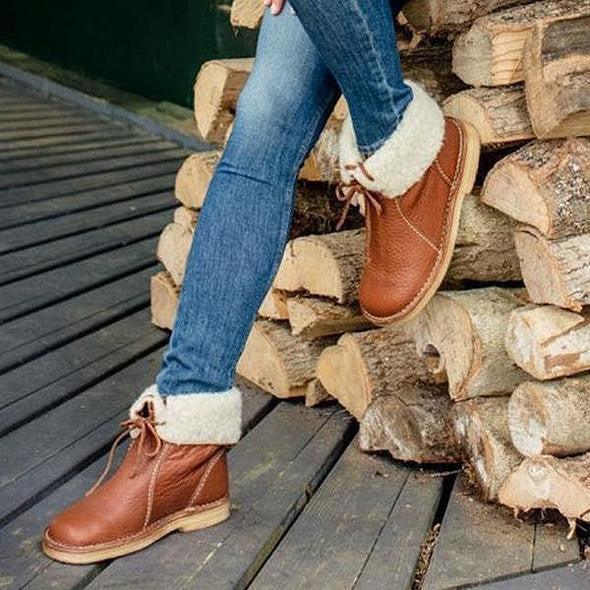 Jeans og brune vinterstøvler med hvidt for, ved siden af stablet brænde. Komfortable, stilfulde støvler til vintermode.