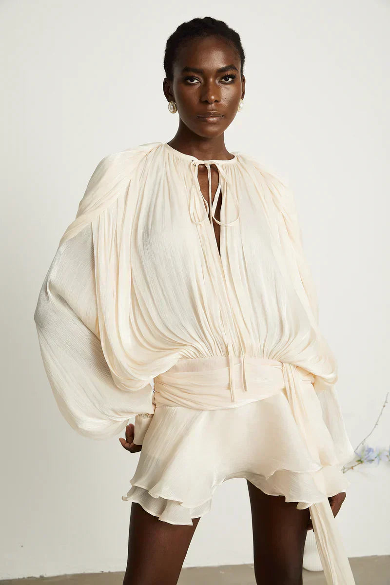 Kvinde iført elegant, hvid kjole med lange ærmer og flæsedetaljer. Moderne mode, stilfuldt design, luksuriøst tøj.