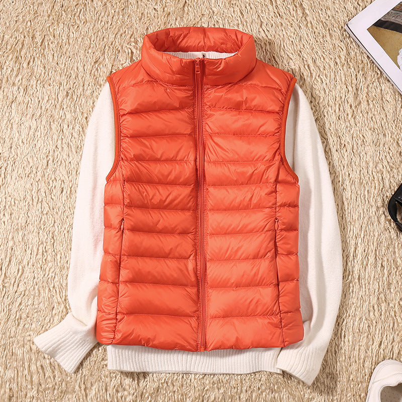 Orange dunvest på hvid sweater, liggende på beige tæppe. Mode, vintertøj, varm vest, stilfuldt design, udendørs beklædning.