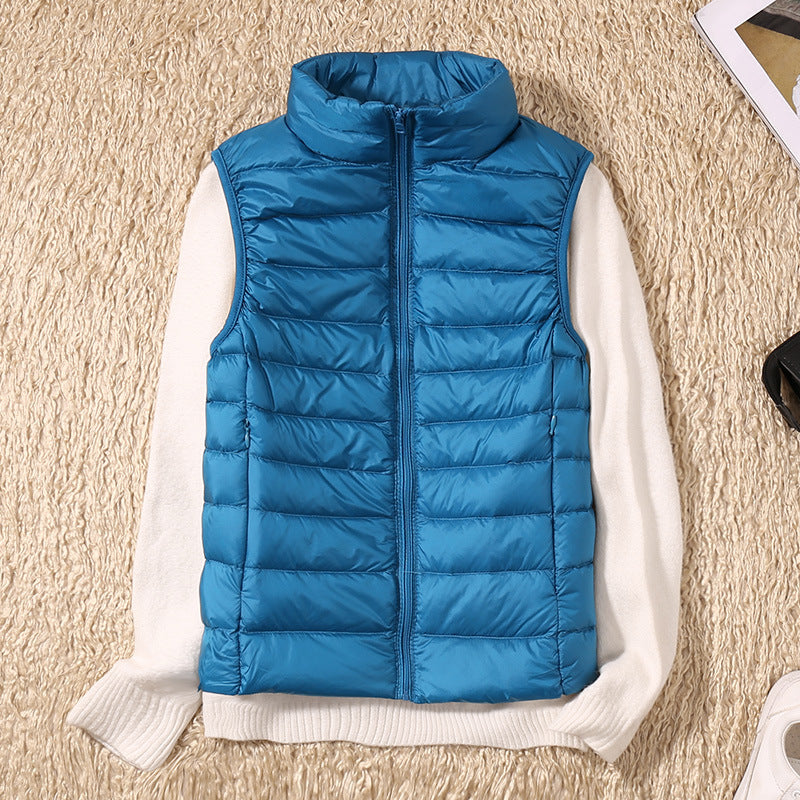 Blå dunvest på hvid sweater, liggende på beige tæppe. Mode, vintertøj, varm vest, stilfuldt design, udendørs beklædning, casual look.