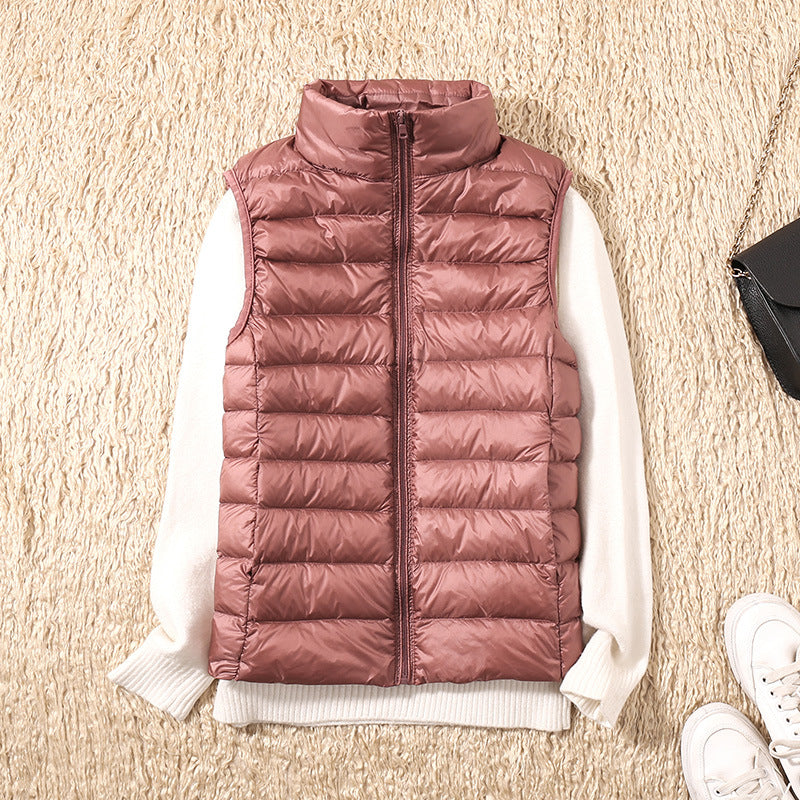 Brun dunvest til kvinder på beige tæppe, med hvid sweater under. Mode, vintertøj, damebeklædning, stilfuld og varm vest til kolde dage.