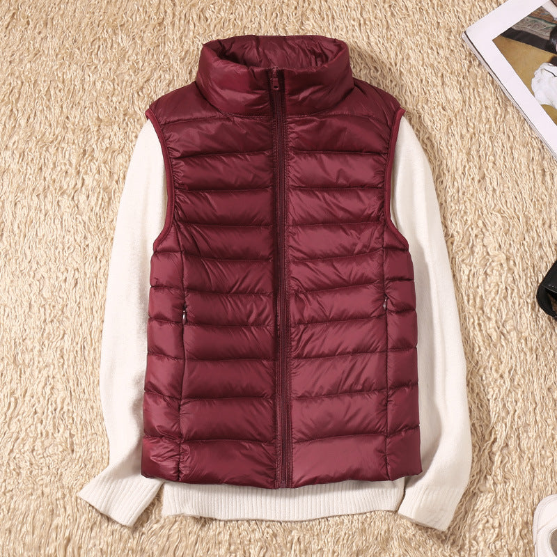 Bordeaux dunvest på hvid sweater, liggende på beige tæppe. Mode, vintertøj, stilfuld vest, varm beklædning, udendørs påklædning.