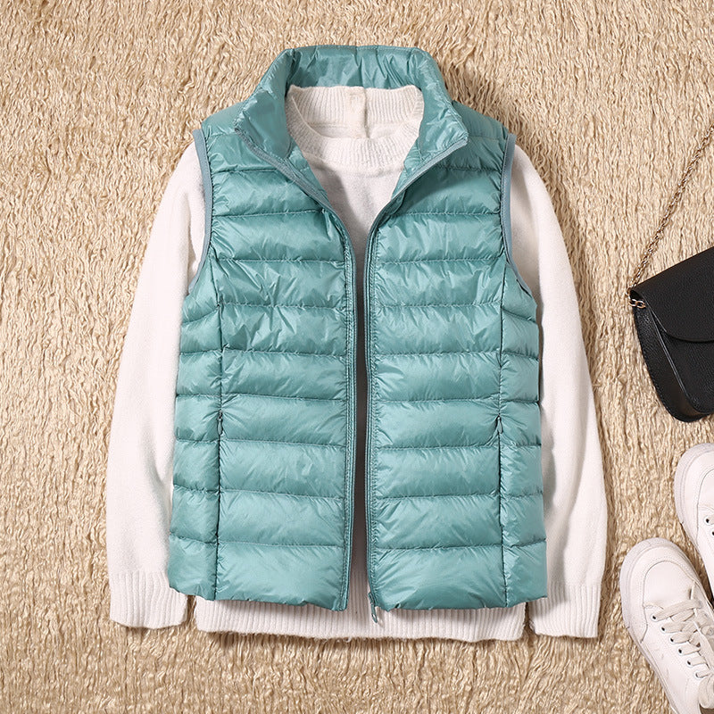 Lyseblå dunvest over hvid sweater på beige tæppe, ved siden af sort taske og hvide sneakers. Mode, vintertøj, casual stil.