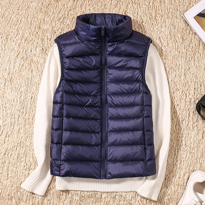 Mørkeblå dunvest på hvid sweater, liggende på beige tæppe. Mode, vinterbeklædning, stilfuld, varm vest til kvinder.