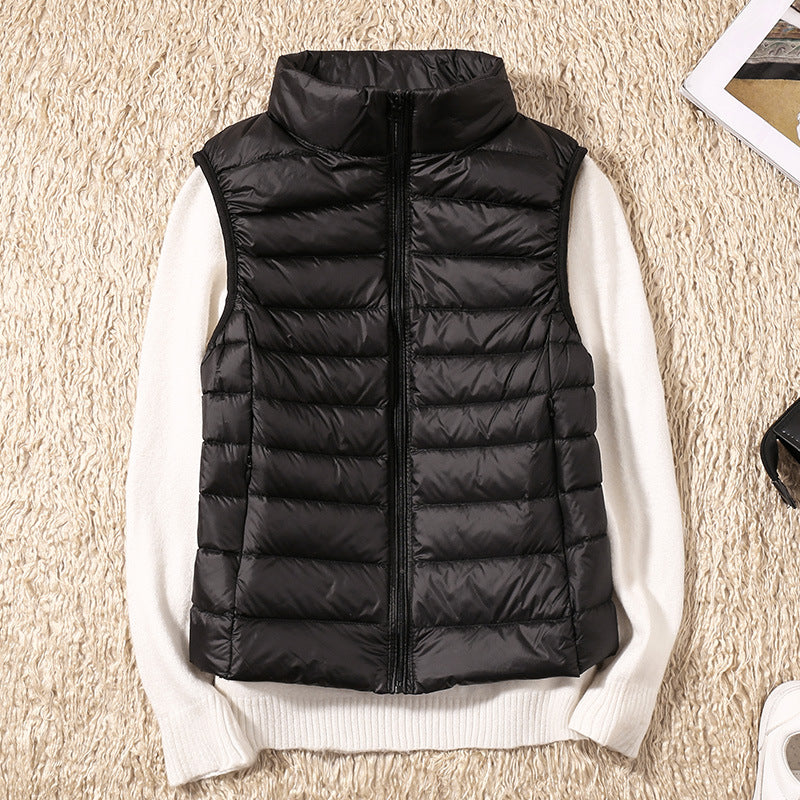 Sort dunvest på hvid sweater, liggende på beige tæppe. Mode, vinterbeklædning, stilfuld, varm vest, kvinders overtøj, moderne design.