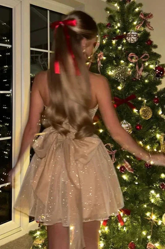 Kvinde i glitrende kjole med rød sløjfe ved juletræ pyntet med lys og kugler. Festlig juleaften, elegant kjole, julepynt, juletræ.