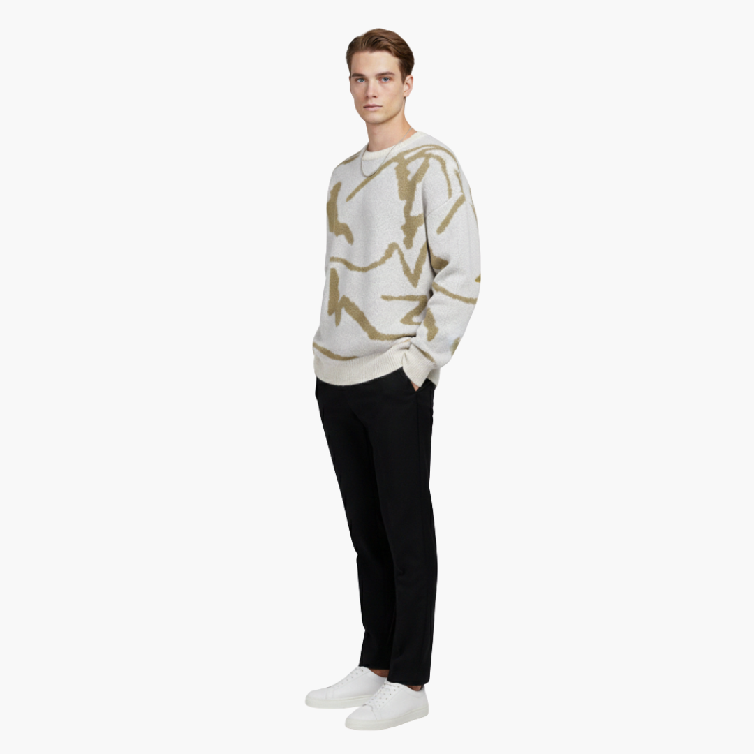 Ung mand iført hvid og beige mønstret sweater, sorte bukser og hvide sneakers. Moderne herremode, afslappet stil, minimalistisk design.