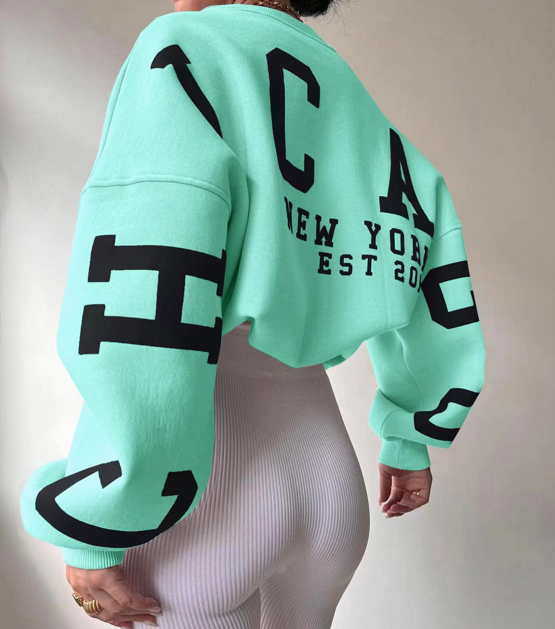 Kvinde iført mintgrøn sweatshirt med sort tekst "New York EST 2020" og store bogstaver. Moderne mode, afslappet stil, trendy tøj.