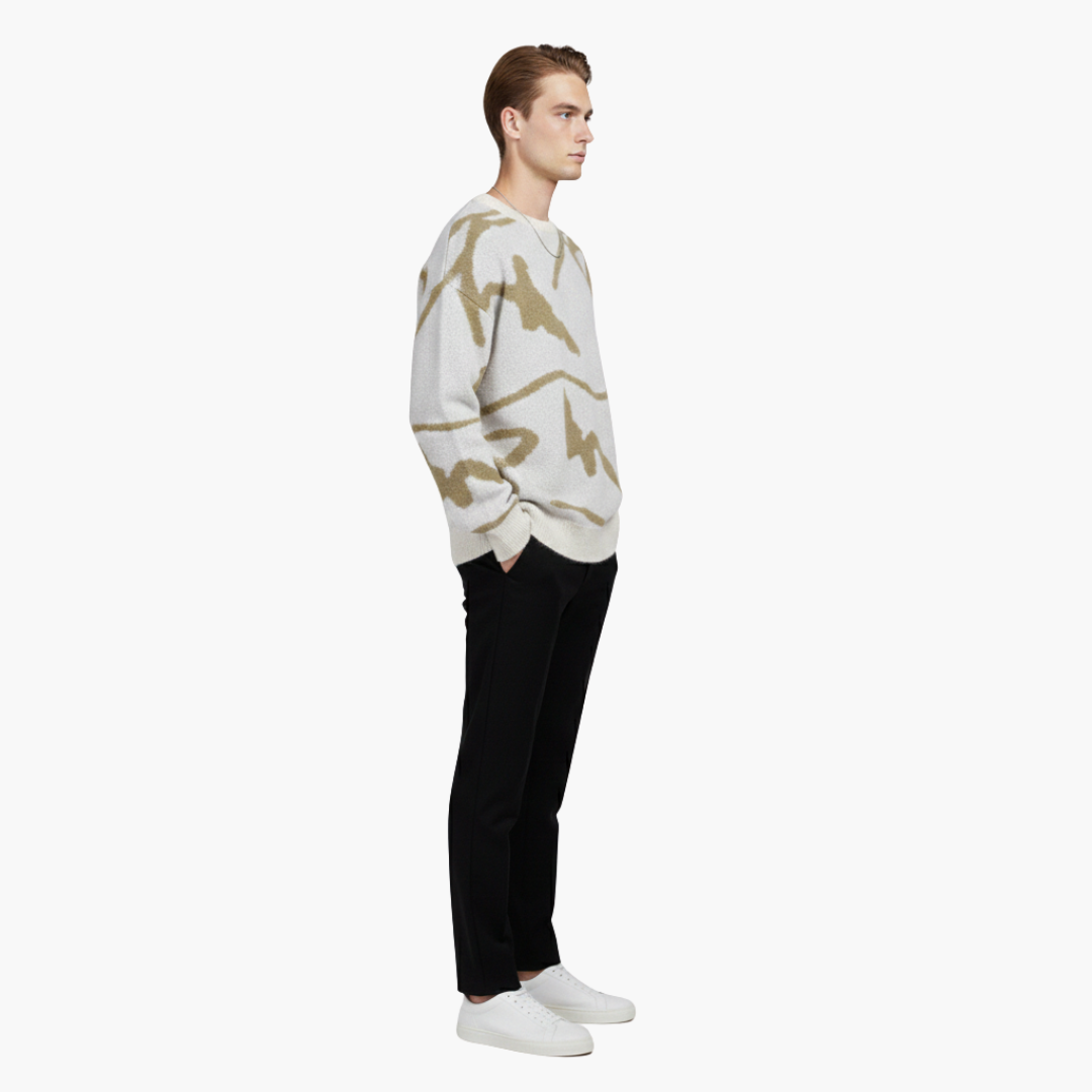 Ung mand iført hvid og beige mønstret sweater, sorte bukser og hvide sneakers. Moderne herremode, afslappet stil, sideprofil.