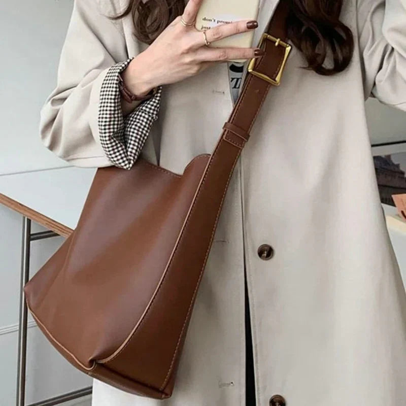 Brun læder skuldertaske bæres af kvinde i beige frakke. Stilfuldt tilbehør, mode, hverdagsbrug, trendy design, praktisk taske.