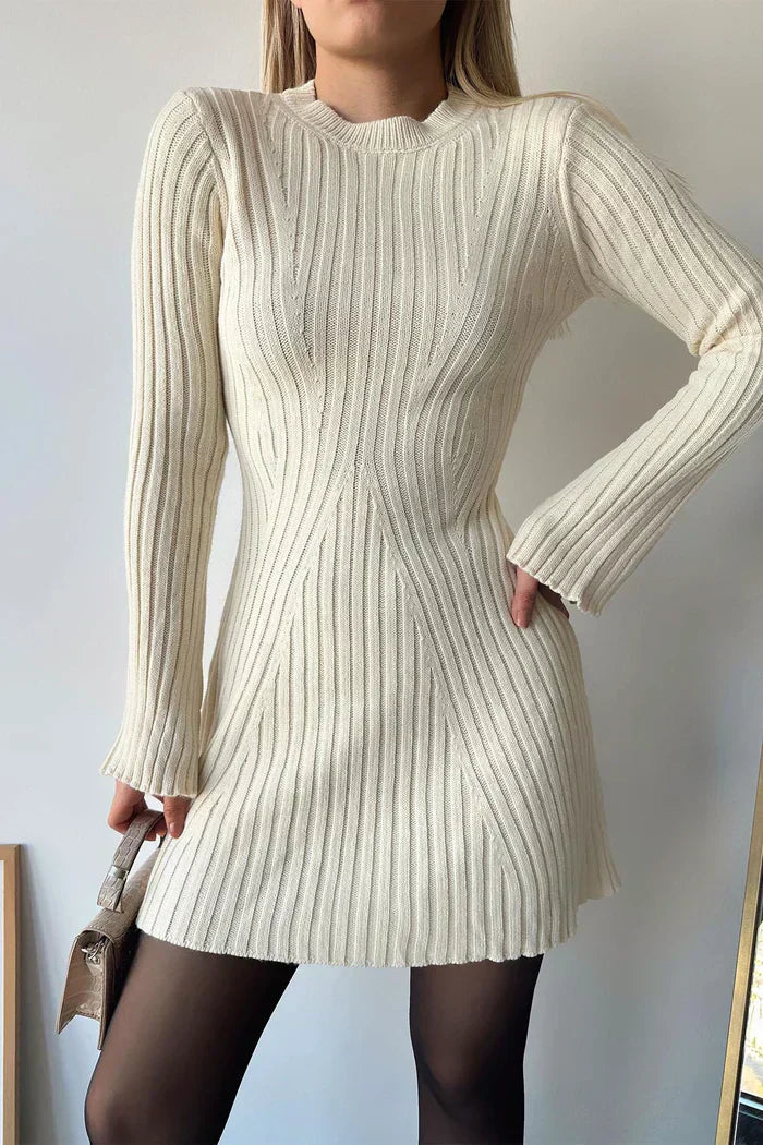 Kvinde iført hvid strikket kjole med lange ærmer, poserer med en lille taske. Elegant vintermode, ribstrikket design, stilfuldt og moderne look.