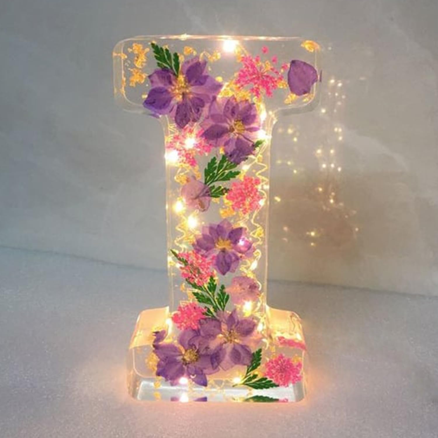 Dekorativt bogstav "I" i gennemsigtigt resin med indlejrede lilla og lyserøde blomster samt LED-lys. Perfekt til boligindretning og gaveidéer.