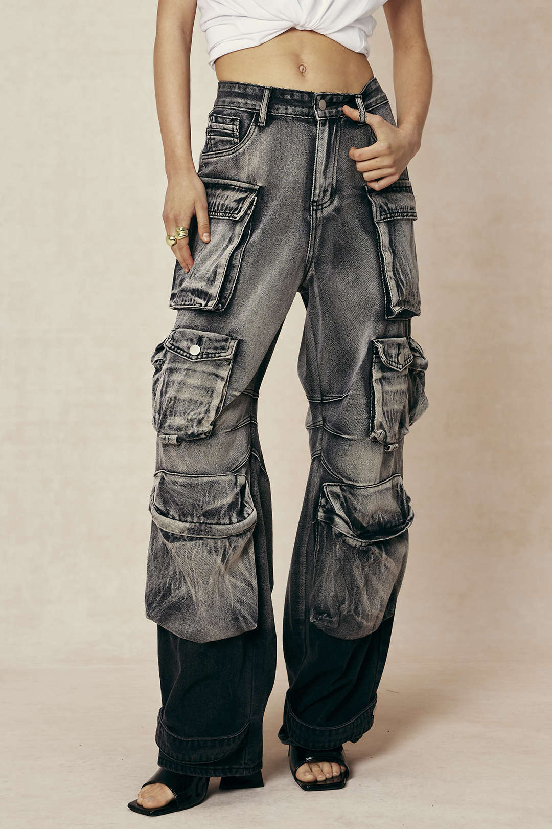 Kvinde iført sorte, slidte cargo-bukser med mange lommer og hvid crop top. Trendy streetwear mode, perfekt til urban stil og afslappet look.