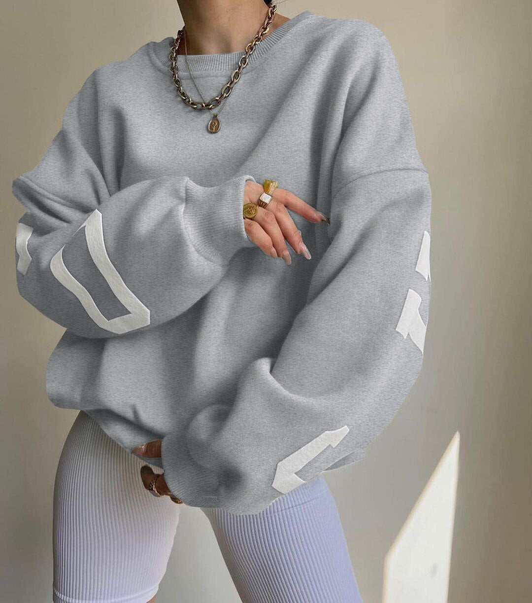 Kvinde iført grå oversized sweatshirt med hvide striber på ærmerne, kombineret med hvide ribbede leggings. Mode, afslappet stil, streetwear.