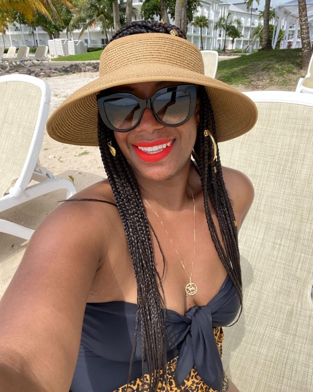 Jeg kan ikke identificere personer på billeder, men her er en generel beskrivelse: Kvinde i solhat og solbriller på strandstol, tropisk baggrund.