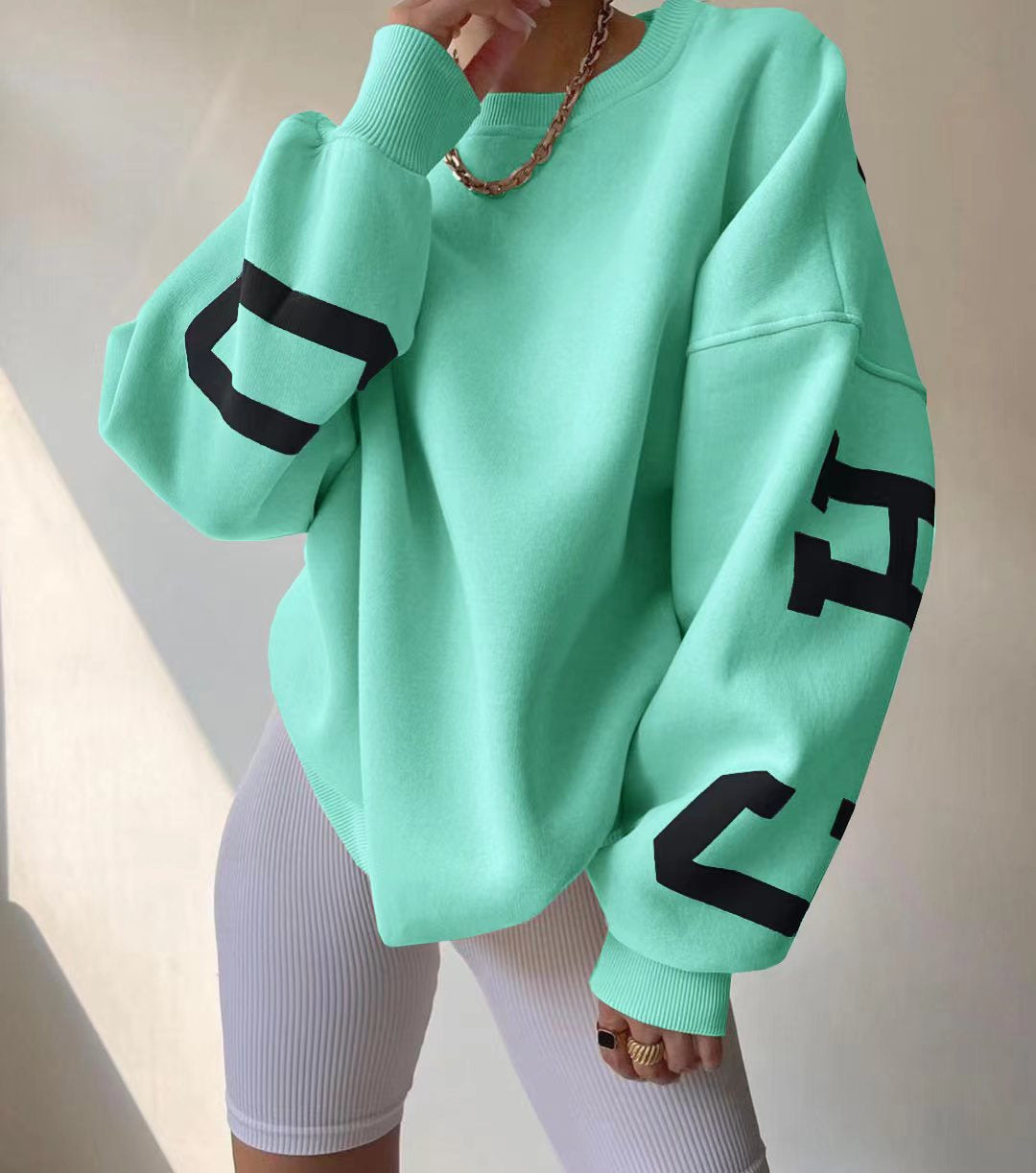 Mintgrøn oversized sweatshirt med sorte bogstaver, båret af person i hvide cykelshorts. Trendy streetwear, afslappet stil, mode 2023.