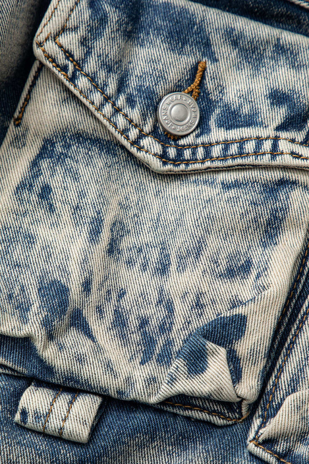 Slidt denimjakke med lomme og metaltrykknap, vintage blåvasket look, teksturdetaljer, mode, jeansstof, close-up.