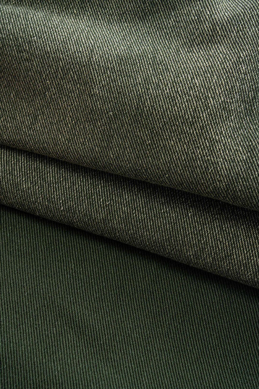 Grøn denimstof i tæt vævning, foldet i lag. Tekstilstruktur, mode, holdbart materiale, tøjdesign.