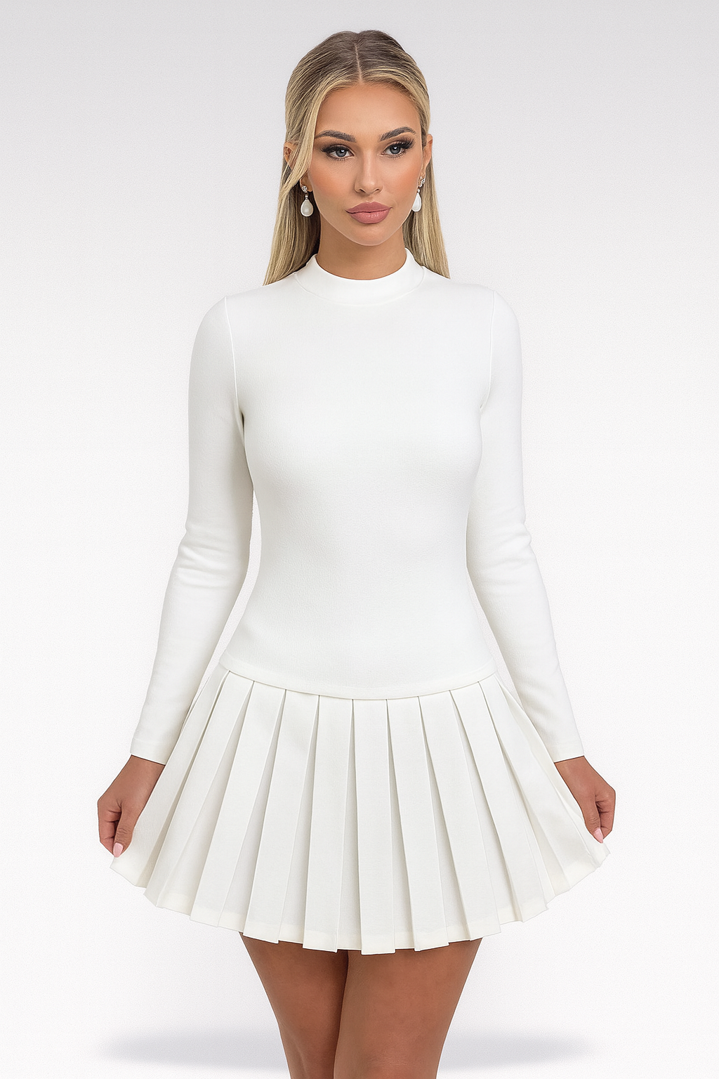 Hvid kjole med lange ærmer og plisseret nederdel, båret af kvinde med langt blondt hår og perleøreringe. Elegant og stilfuldt design.