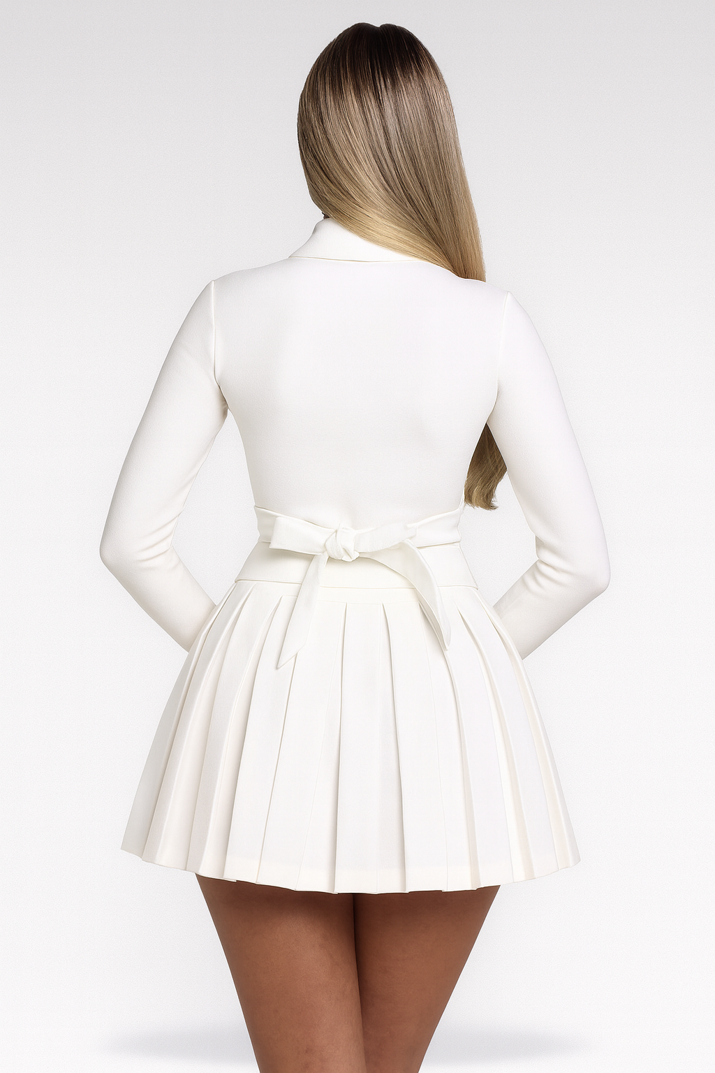 Kvinde i hvid kjole set bagfra, med langt hår og plisseret nederdel. Elegant og stilfuldt outfit til festlige lejligheder.