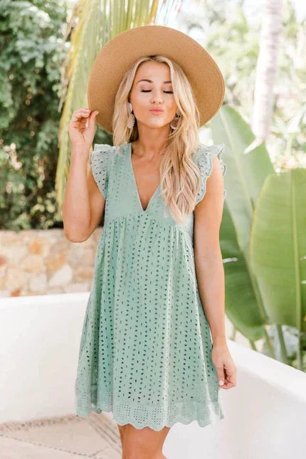 Ung kvinde i mintgrøn sommerkjole og bredskygget hat, står foran tropiske planter. Sommermode, boho-stil, afslappet look.