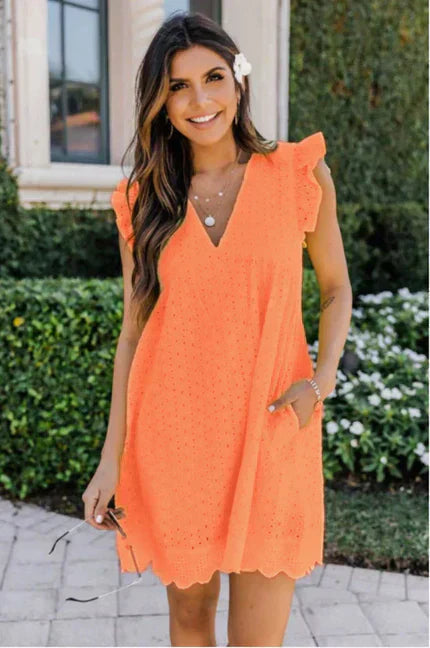 Kvinde i orange sommerkjole med blonder, smilende i have. Kjolen har v-udskæring og lommer. Perfekt til sommermode og afslappet stil.
