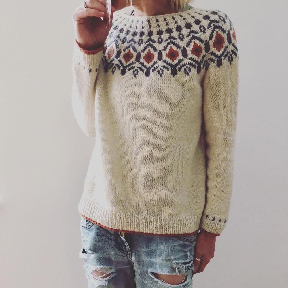 Kvinde iført beige striktrøje med nordisk mønster og slidte jeans. Trendy vintermode, skandinavisk design, casual stil.