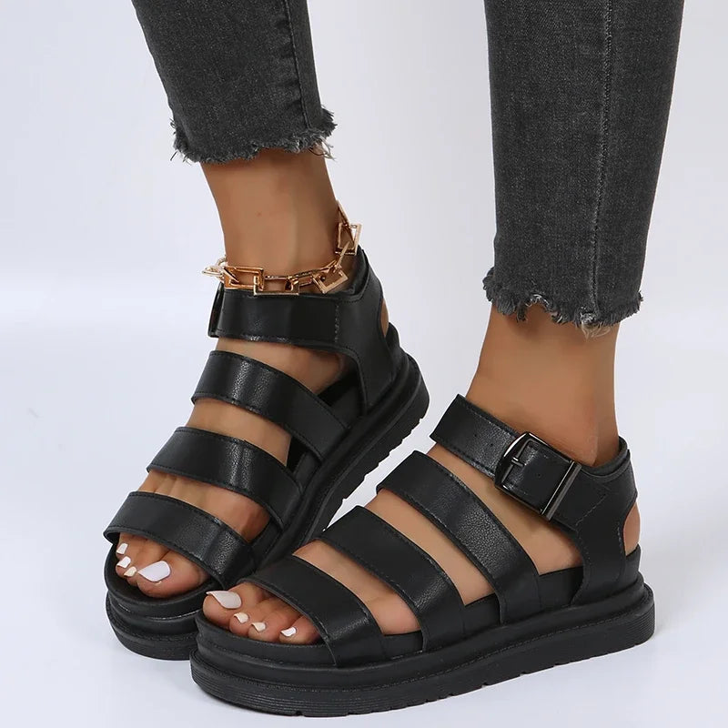 Sort læder sandaler med remme og spænde, båret af person i grå jeans. Trendy fodtøj til sommermode. Komfortable og stilfulde damesandaler.