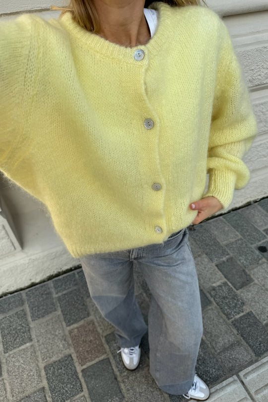 Kvinde iført gul striktrøje med knapper, grå jeans og hvide sneakers. Mode, street style, afslappet outfit, trendy tøj til efterår.