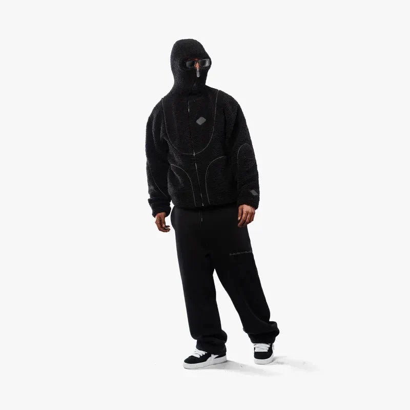 Sort hættetrøje og bukser, ansigtsmaske, sneakers. Streetwear mode, urban stil, moderne tøj, afslappet look, sort outfit, minimalistisk design.