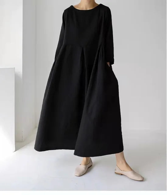 Sort, langærmet kjole i minimalistisk design, bæres af en person i lyse flade sko. Perfekt til skandinavisk mode og tidløs stil.