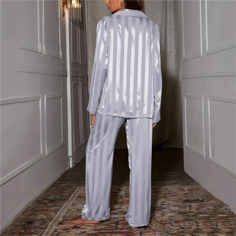 Kvinde iført stribet, sølvfarvet satinpyjamas i elegant gang. Komfortabelt nattøj, luksuriøst design, moderne stil, perfekt til afslapning.