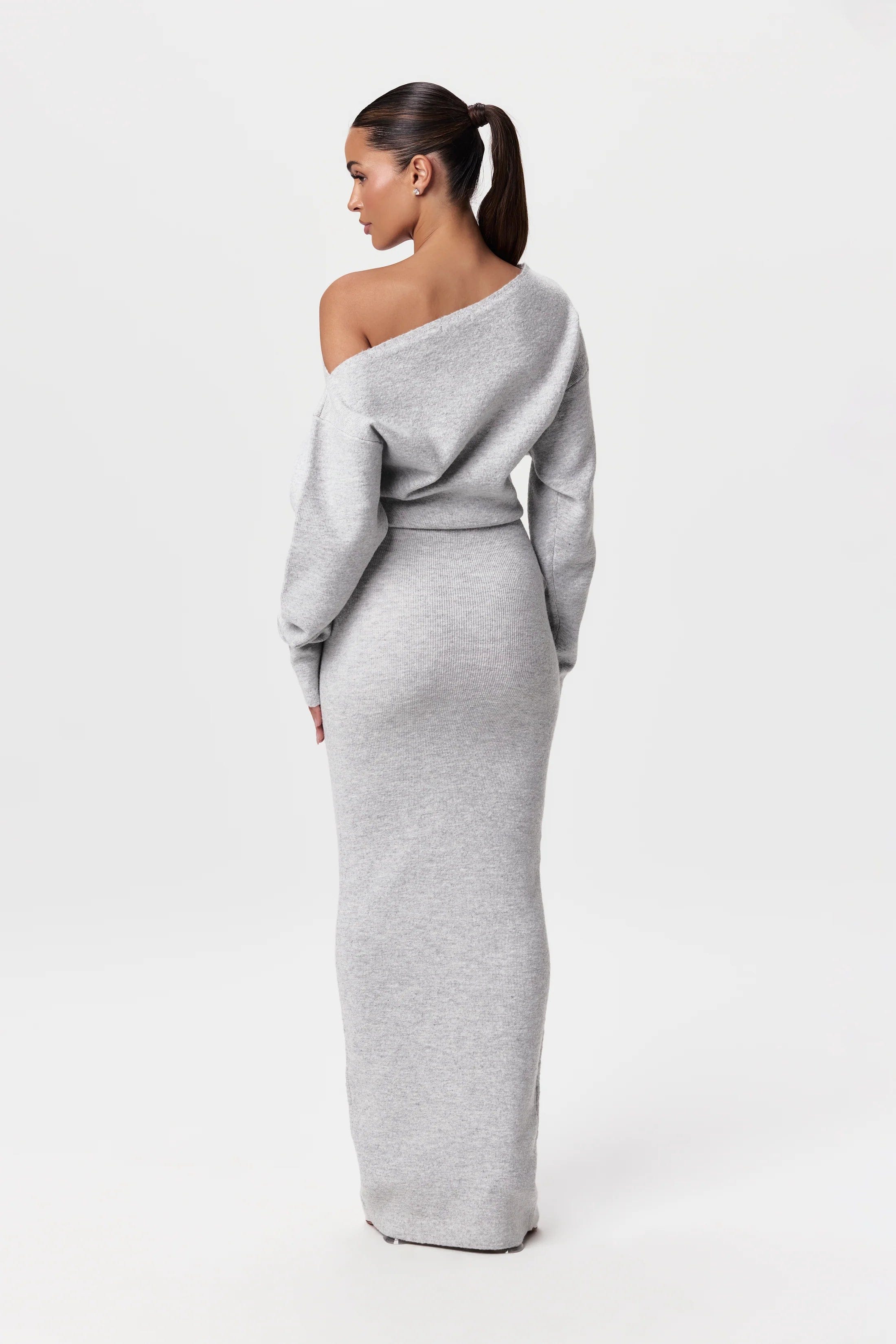 Kvinde i grå, off-shoulder kjole med langt ærme og tætsiddende pasform. Elegant og moderne mode, perfekt til stilfulde lejligheder.