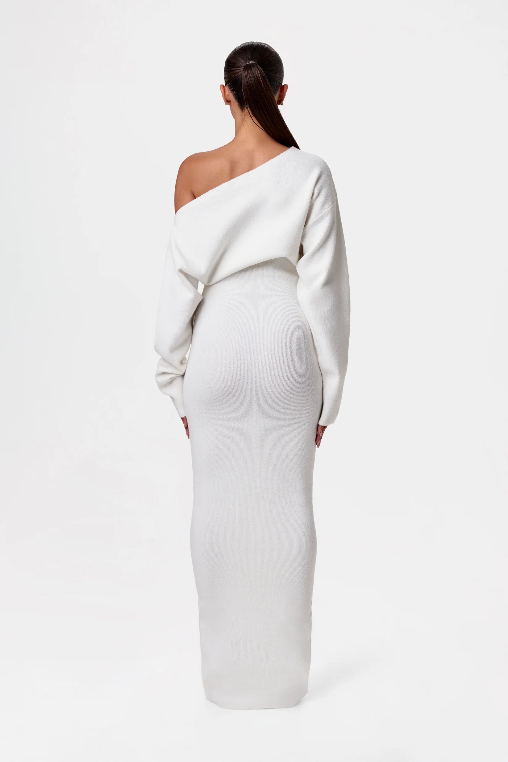 Kvinde i hvid, asymmetrisk, langærmet kjole set bagfra. Elegant, minimalistisk design, perfekt til modebevidste kvinder.