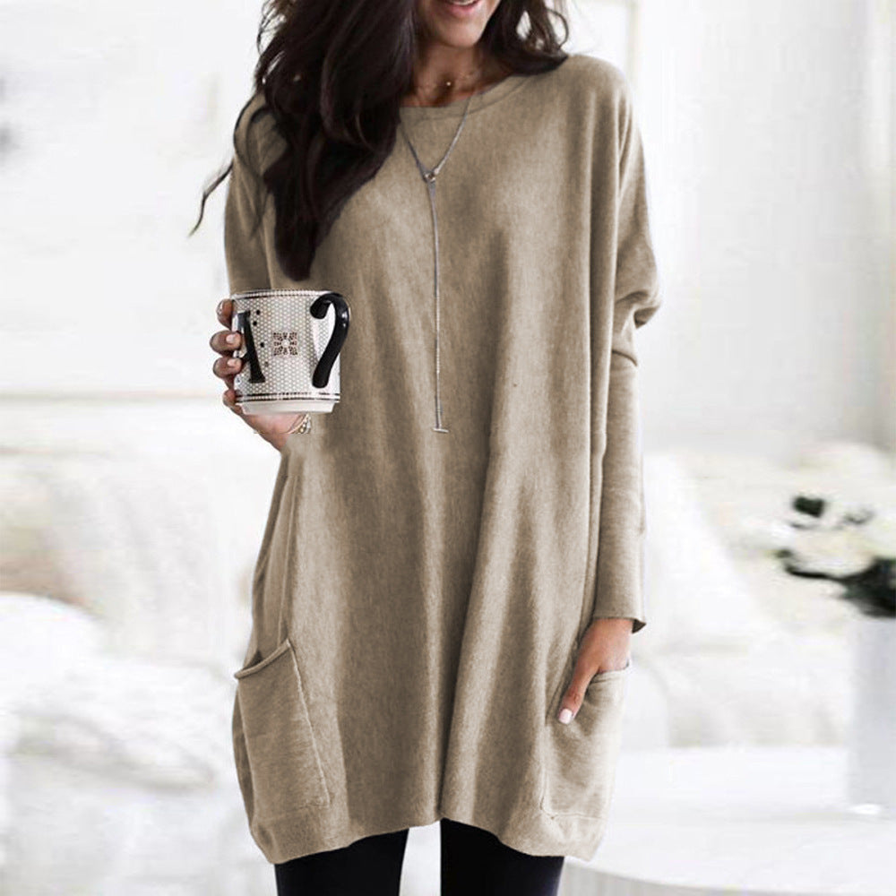 Kvinde iført beige oversized sweater med lommer, holder en kaffekop. Stilfuldt afslappet look, perfekt til efterårsmode og hygge derhjemme.