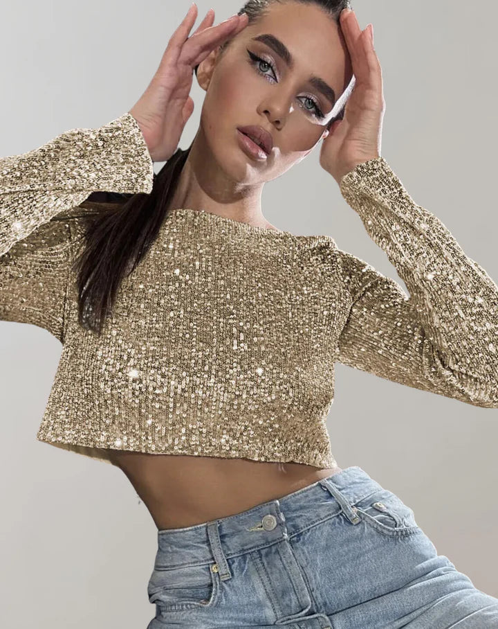 Kvinde i glitrende guldtrøje og blå jeans poserer mod grå baggrund. Mode, glamour, stilfuldt outfit, moderne kvindetøj.