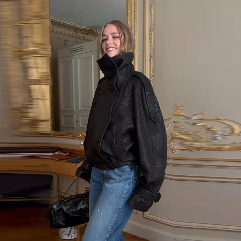 Kvinde iført sort læderjakke og blå jeans i elegant rum med gyldne detaljer. Mode, stilfuldt tøj, moderne design, indendørs.
