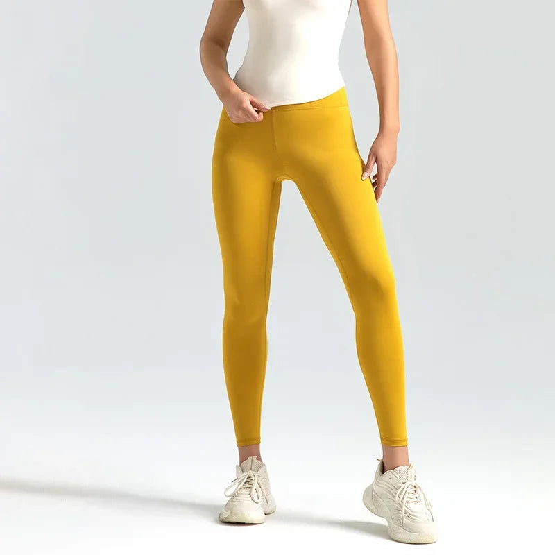 Kvinde iført gule leggings og hvide sneakers mod en neutral baggrund. Komfortabelt og stilfuldt sportstøj til træning eller afslappet brug.
