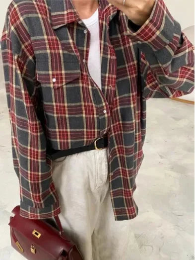 Person iført rødternet skjorte over hvid T-shirt, beige bukser og bærer en rød taske. Casual mode, efterårslook, trendy outfit.