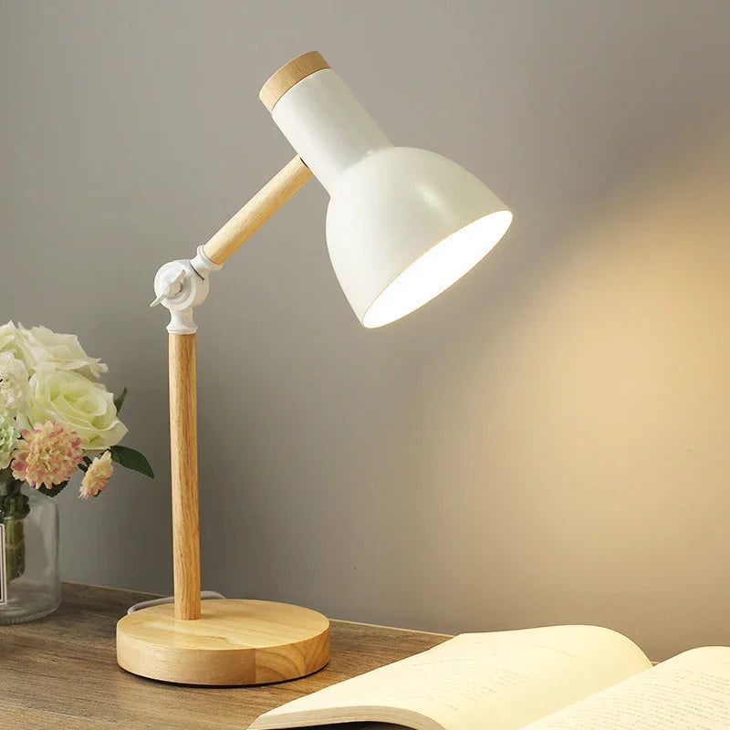 Hvid skrivebordslampe med trædetaljer lyser op på et træbord ved siden af en åben bog og en vase med blomster. Moderne belysning til hjemmekontor.