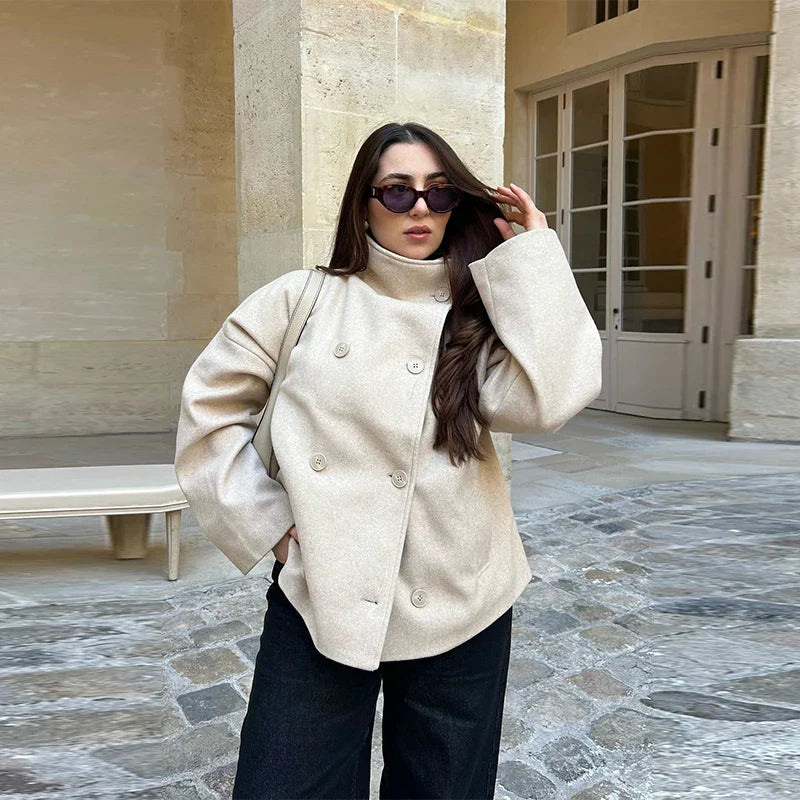 Kvinde i beige frakke og solbriller står på brostensbelagt gårdsplads. Mode, efterårstøj, stilfuldt look, udendørs.