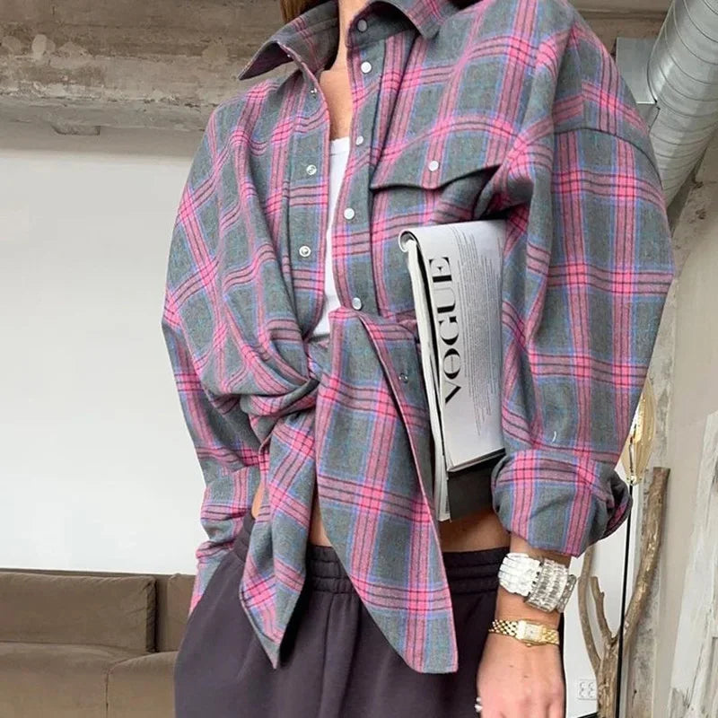 Kvinde i ternet skjorte med Vogue-magasin under armen, iført sort bukser og sølvur. Moderne mode, afslappet stil, indendørs miljø.