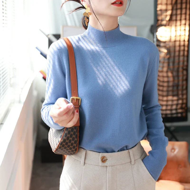 Kvinde i blå sweater og beige bukser, bærer en brun skuldertaske. Moderne mode, elegant stil, indendørs belysning.
