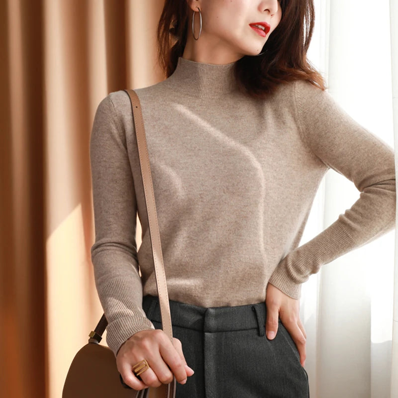 Kvinde i beige rullekrave og grå bukser, bærer brun skuldertaske. Elegant efterårsoutfit, moderne mode, stilfuldt tøj til kvinder.