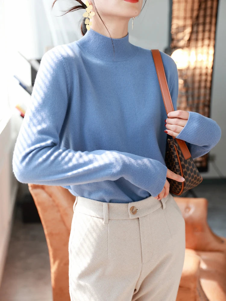 Kvinde i blå sweater og beige bukser, bærer en brun skuldertaske. Moderne mode, elegant stil, indendørs belysning, trendy accessories.
