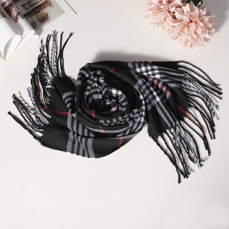Sort og hvidternet tørklæde med røde striber, liggende på hvid overflade ved siden af lyserøde blomster. Elegant modeaccessory til vinter.