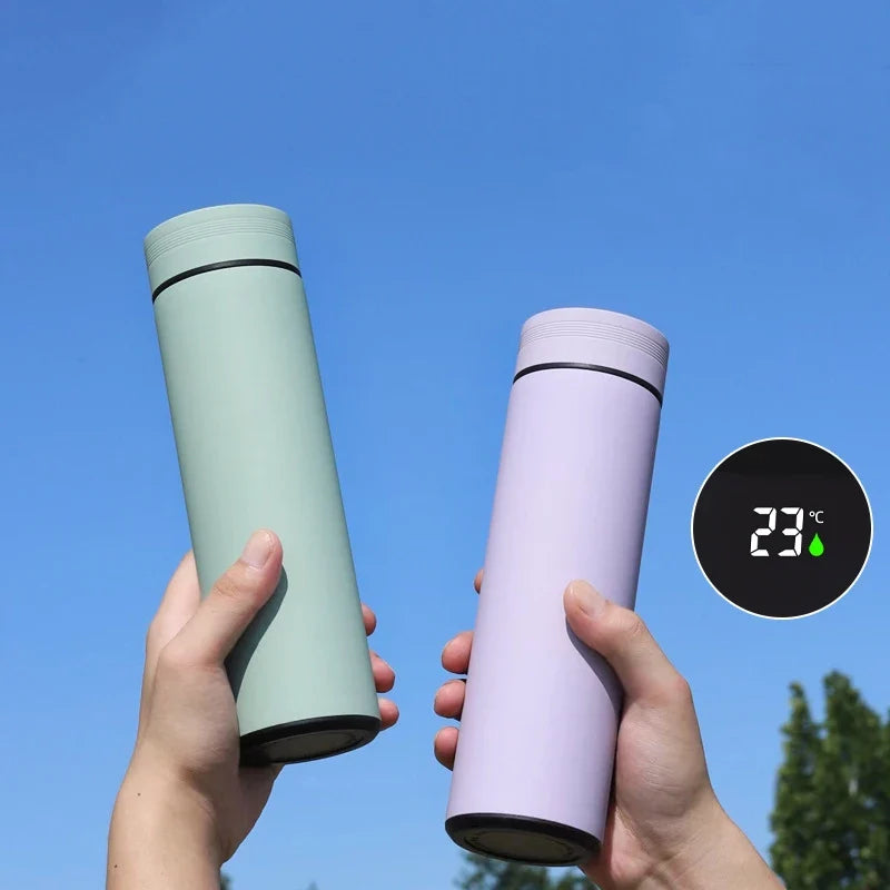 To termokrus i pastelgrøn og lilla holdes op mod en blå himmel. Digital temperaturvisning på 23°C. Miljøvenlig, bærbar termoflaske.